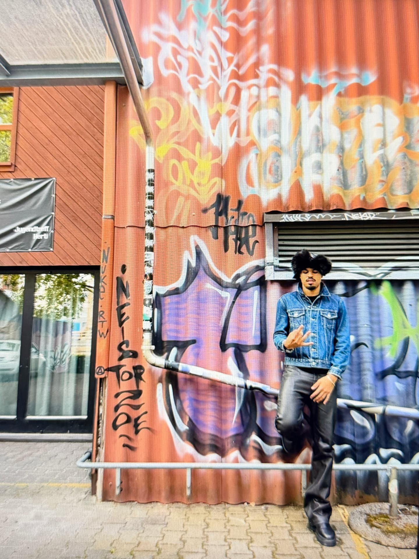 Jaywakeup in a denim jacket standing against a large graffiti-covered corrugated wall