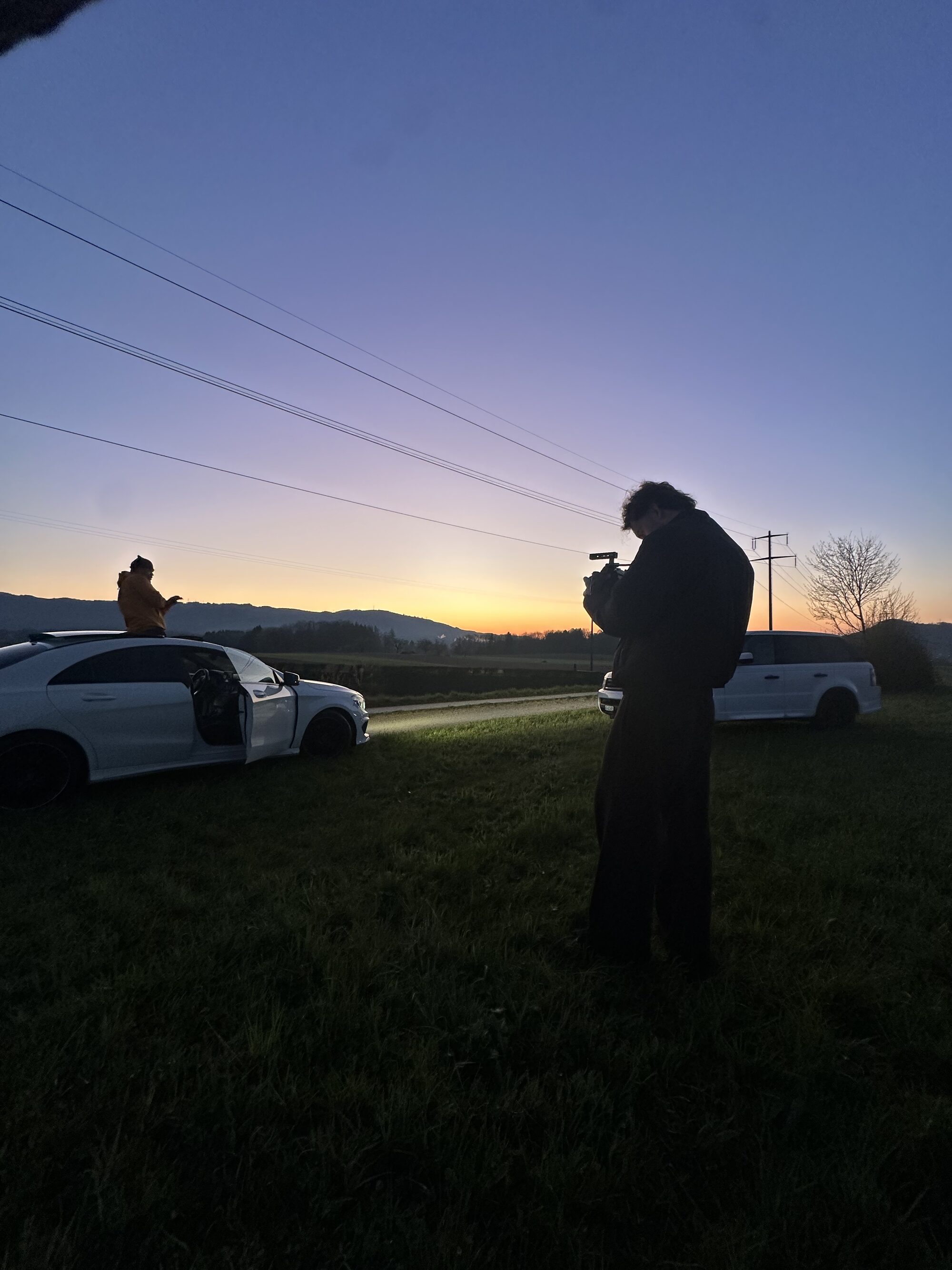 A camera operator filming Jaywakeup on a car roof against a violet dusk sky
